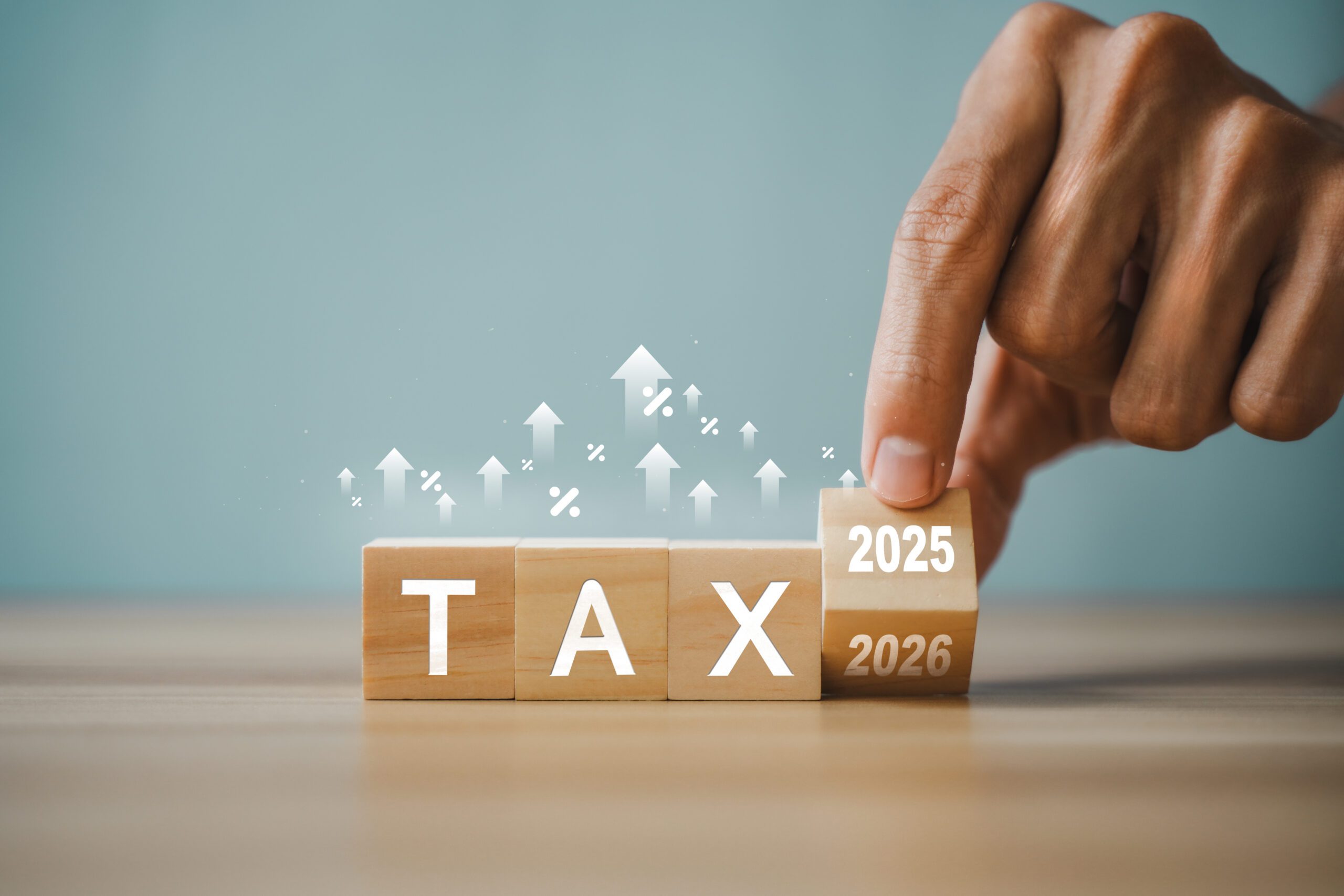 Hand placing a block labeled 2025 above wooden blocks spelling TAX and 2026, representing tax planning and future tax strategy.