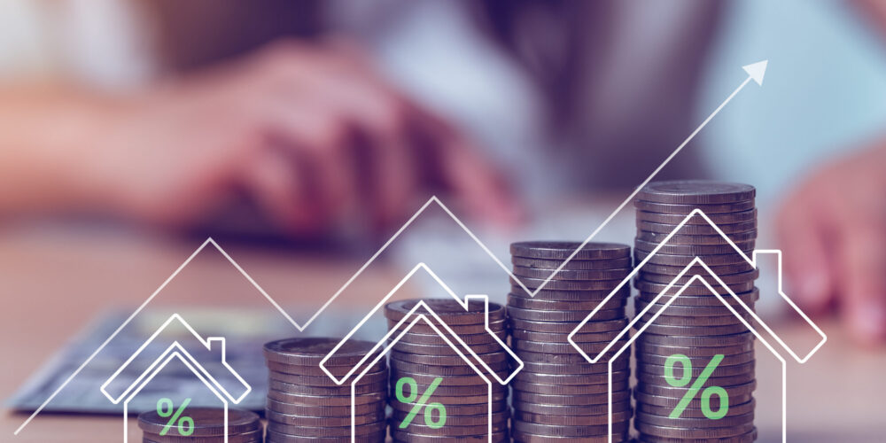 Ascending stacks of coins with percentage symbols and an upward arrow representing rising interest rates